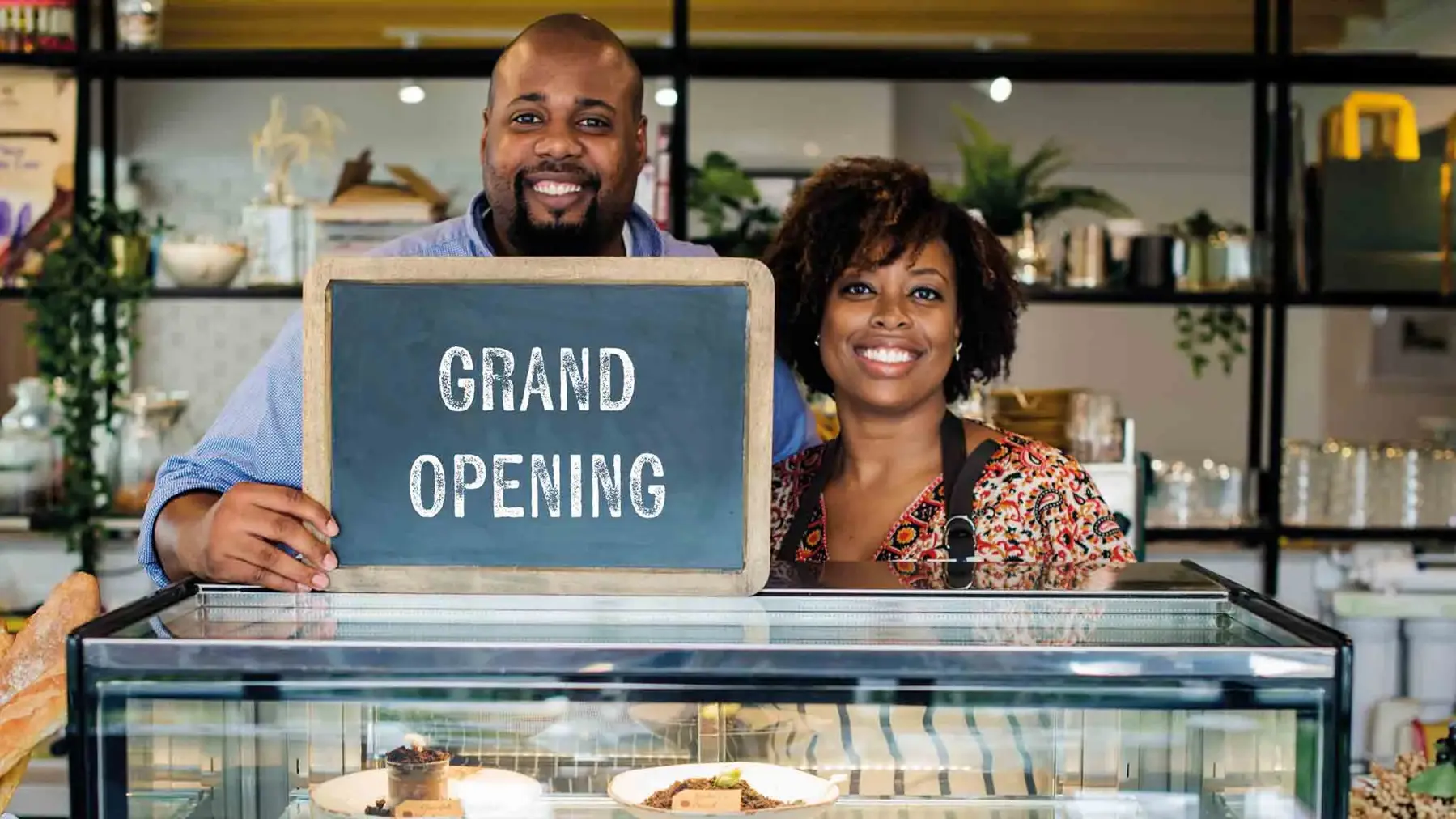 Couple holding up a sign saying 'grand opening' in a restaurant